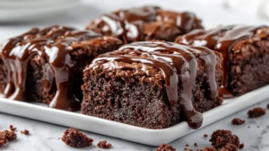 Hyper-realistic photo of thick hot fudge brownies cut into rich square pieces, glossy warm hot fudge poured over the top, dense fudgy brownie texture with shiny chocolate surface, a few clean brownie crumbs on a white marble countertop, one brownie square slightly pulled forward to show the moist chocolate center, soft natural window light, bright white kitchen background, editorial food photography, realistic chocolate shine, cozy dessert styling, shallow depth of field, crisp focus, no people, no hands, no text, no logos, no watermark
