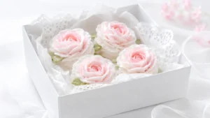 White gift box filled with pale pink and white zefir marshmallow flowers, lace paper, and soft green leaves.